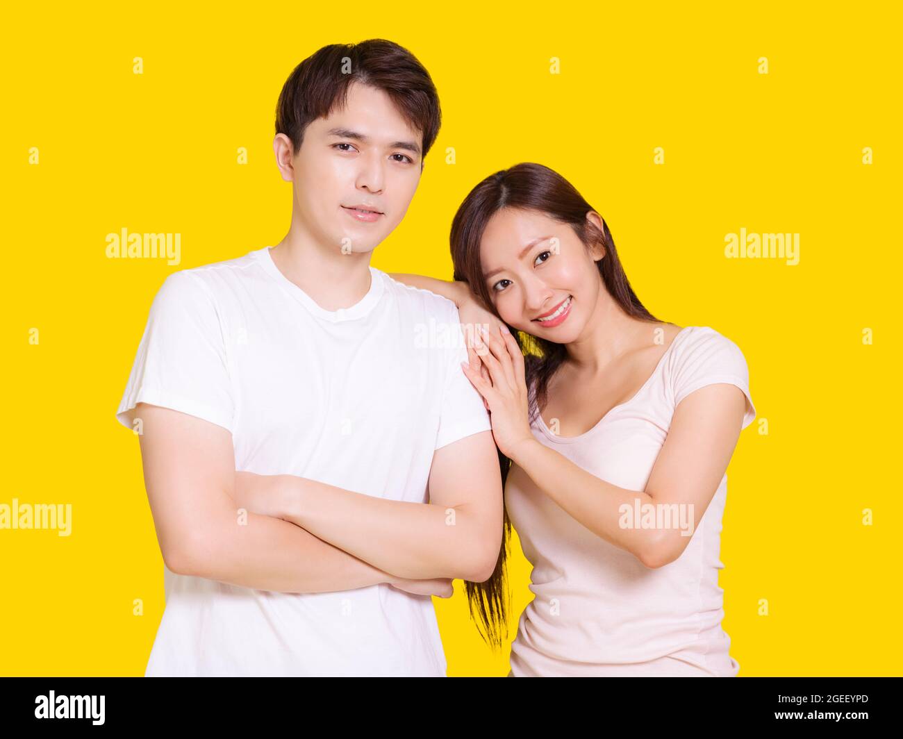 Young couple smiling at camera while woman putting her head on male shoulder .Isolated over yellow background. Stock Photo