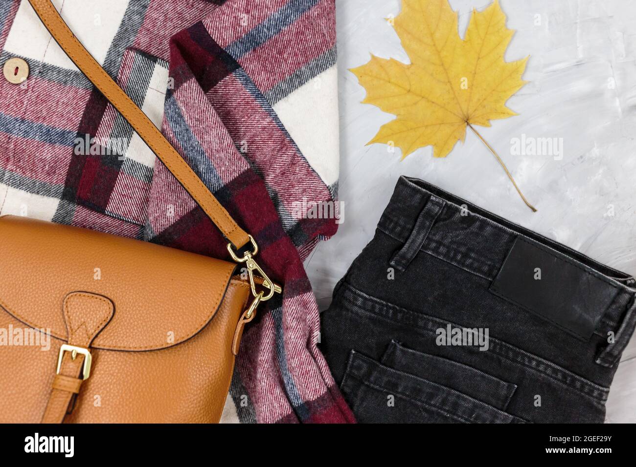Autumn leaves, boots, jeans, leather bag, checkered shirt on gray table. Trendy fashion Autumn accessories, female look Stock Photo