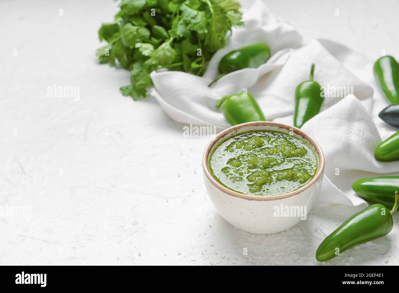 Bowl of Tomatillo Salsa Verde sauce and jalapeno pepper on light background Stock Photo