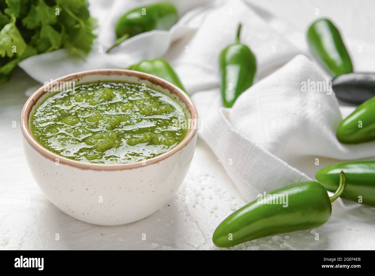 Bowl of Tomatillo Salsa Verde sauce and jalapeno pepper on light background Stock Photo