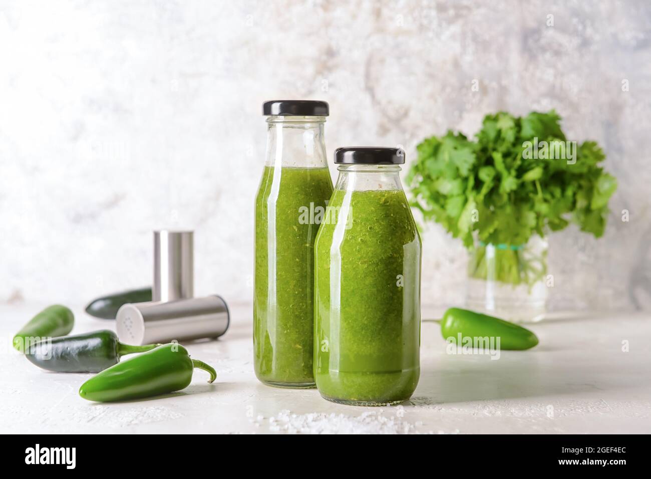 Bottles of Tomatillo Salsa Verde sauce and jalapeno pepper on light background Stock Photo