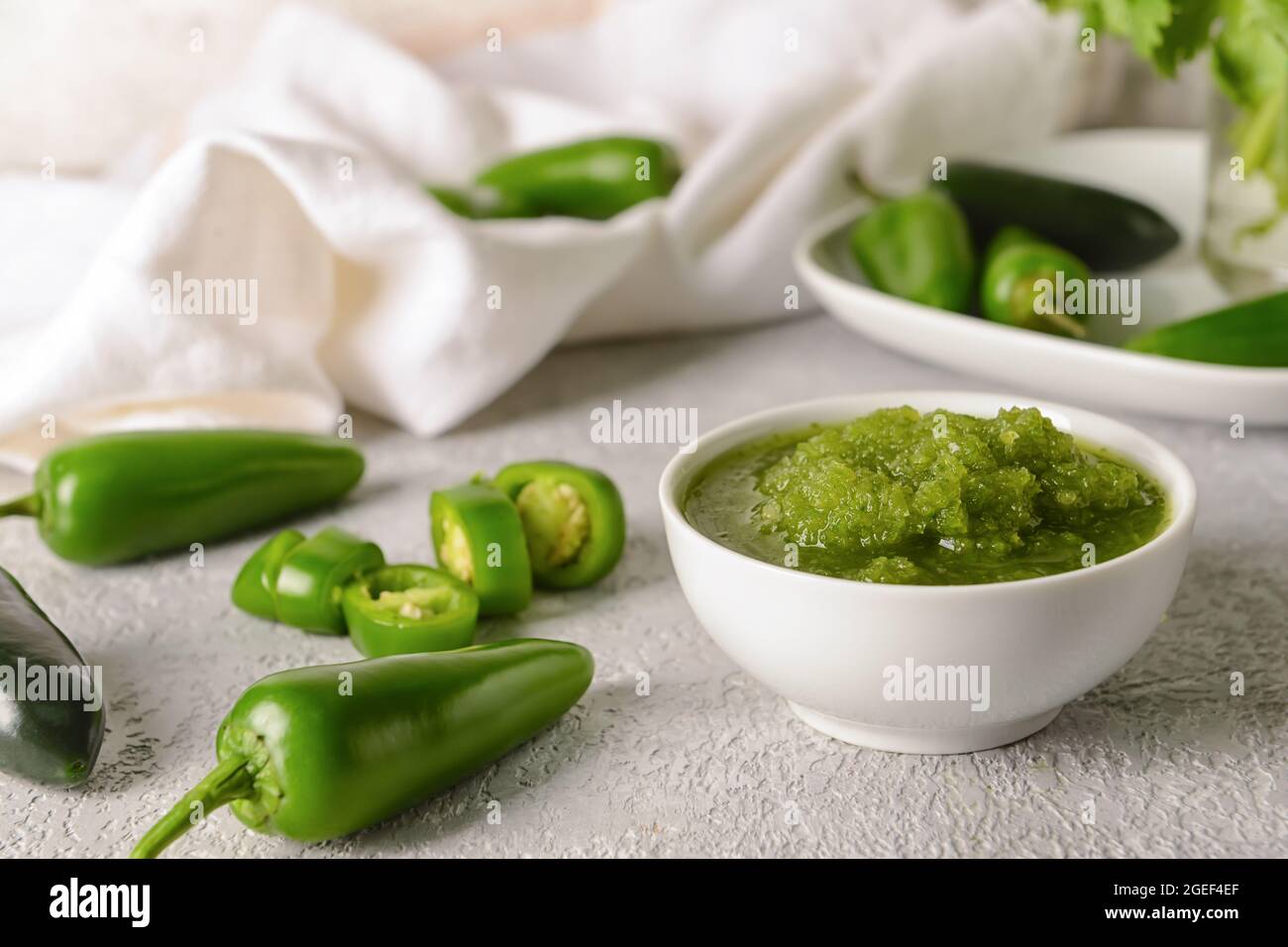 Bowl of Tomatillo Salsa Verde sauce and jalapeno pepper on light background Stock Photo