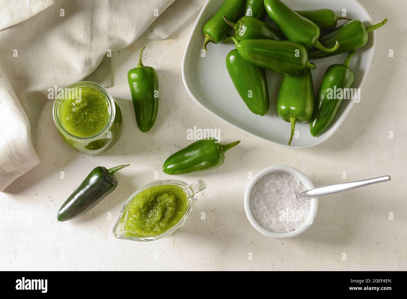 Glass jar and jug with Tomatillo Salsa Verde sauce and ingredients on light background Stock Photo