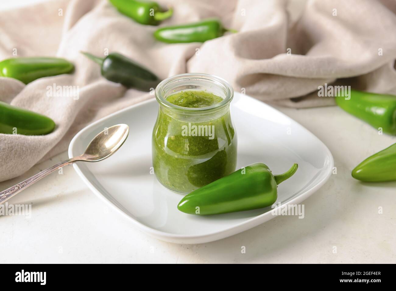 Glass jar of Tomatillo Salsa Verde sauce and jalapeno pepper on light background Stock Photo