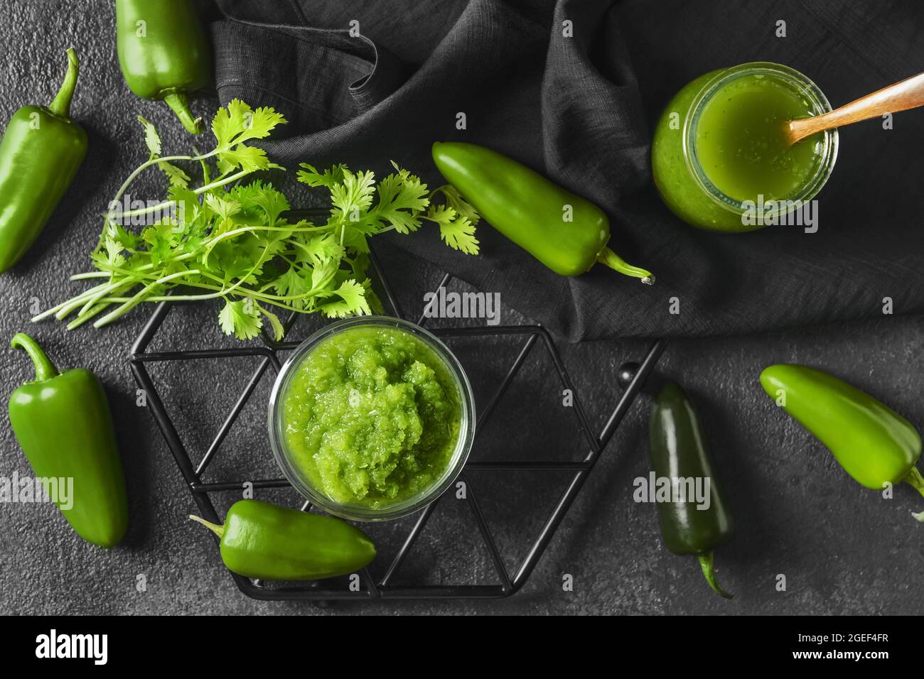 Glass jar and bowl with Tomatillo Salsa Verde sauce and ingredients on dark background Stock Photo