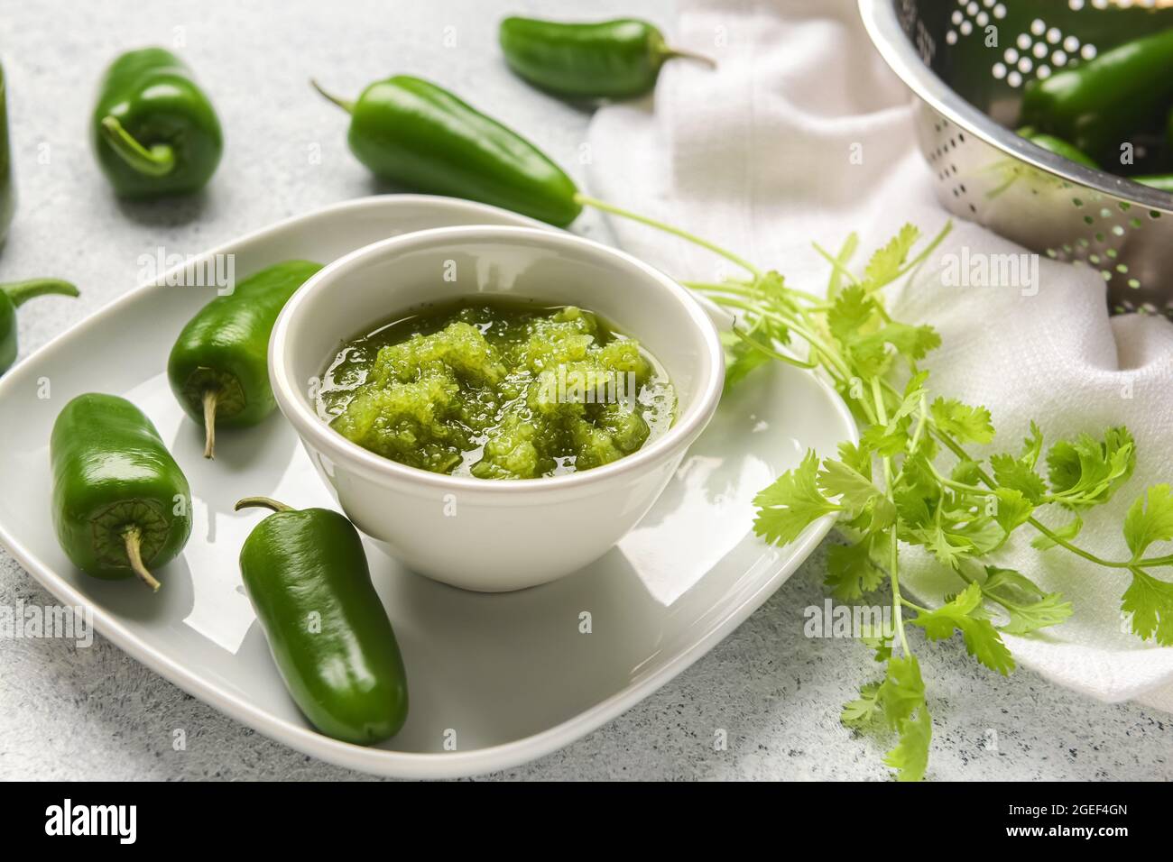 Bowl of Tomatillo Salsa Verde sauce and jalapeno pepper on light background Stock Photo