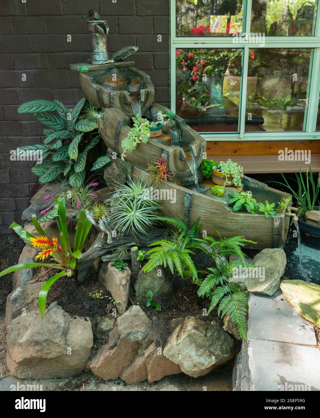 Decorative garden water feature, waterfall with water trickling over old wooden barrels on a rockery with ferns and bromeliads, in Australia Stock Photo