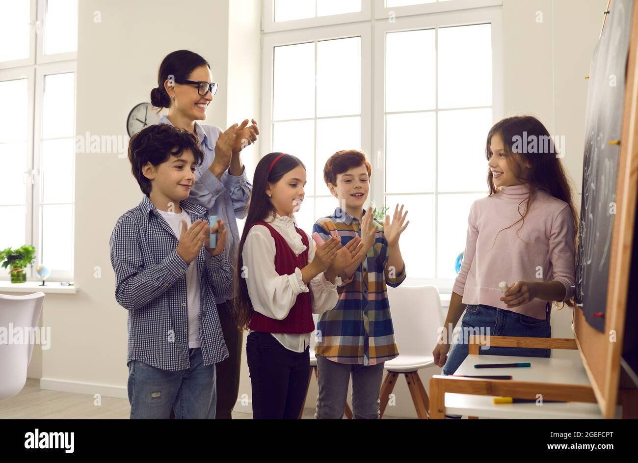 Teacher and pupils congratulate classmate for right answer at blackboard Stock Photo