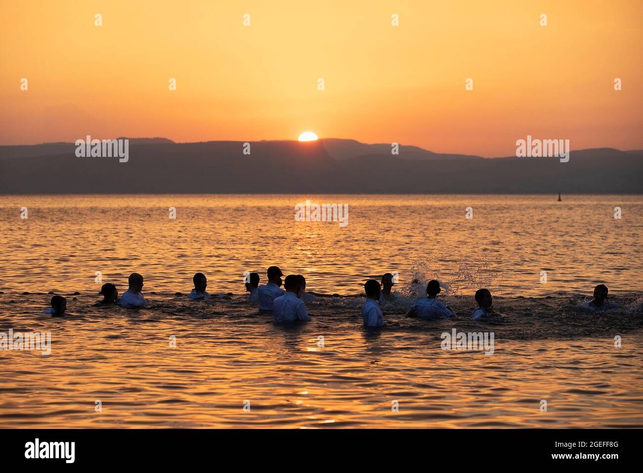 Ultra Orthodox Jewish schoolboys enjoying the evening together while splashing around during a dip in the Sea of Galilee at sunset Stock Photo