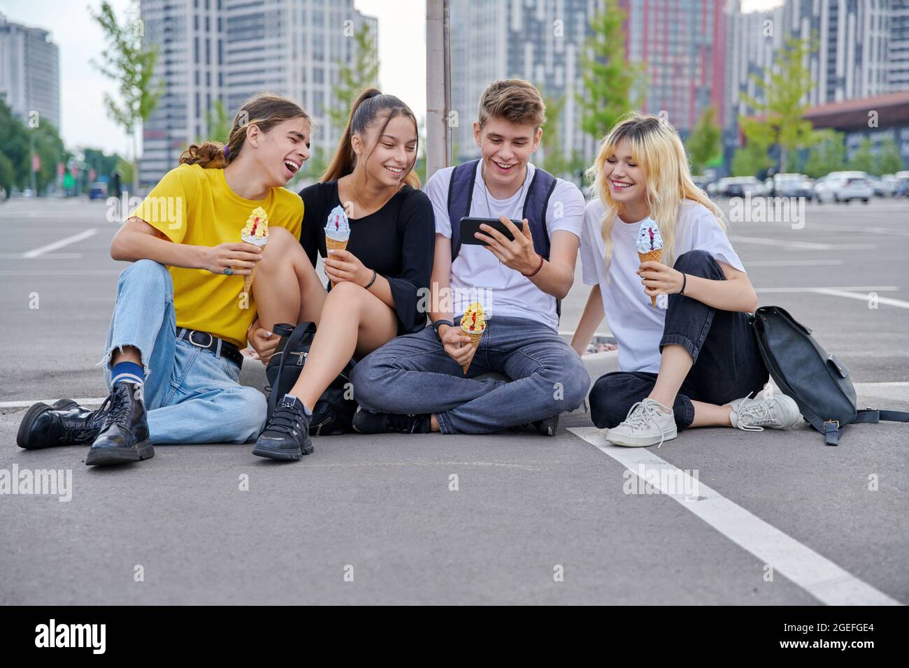 Group of teenagers with ice cream looking together at smartphone, urban style Stock Photo