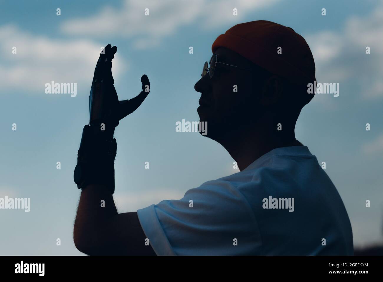 Young disabled man with artificial prosthetic hand silhouette against sky Stock Photo