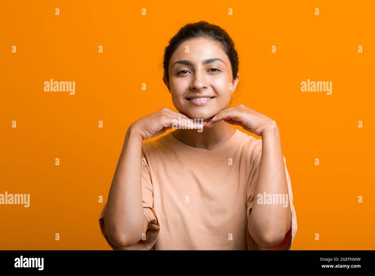 Close up portrait of young indian american woman touching face skin her hands and doing self yoga face gymnastics massage orange background Stock Photo