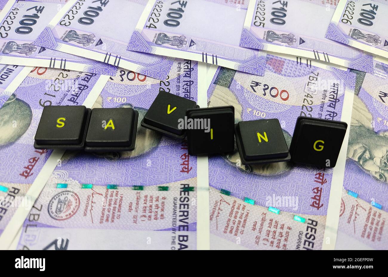 Top view shot of a group of keycaps spelling 'Saving' lying on Indian currency money Stock Photo