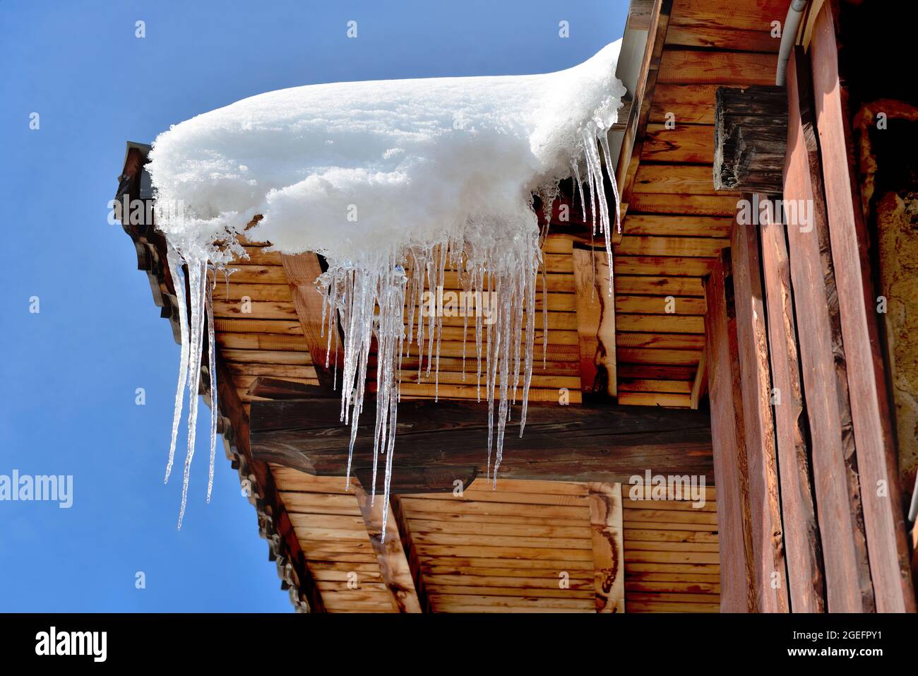roof of wooden house in alpine village covered with snow and icicles ...