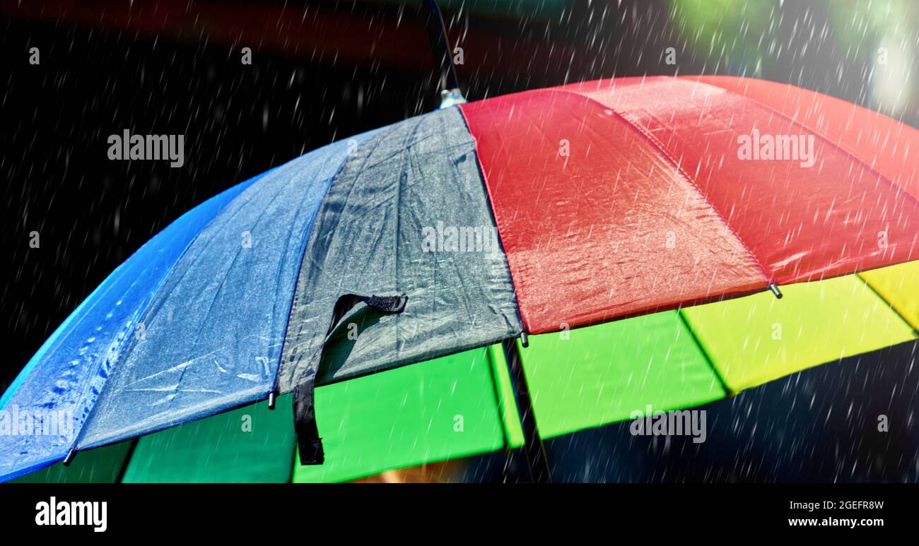Umbrella in the colors of the rainbow during a rain shower Stock Photo