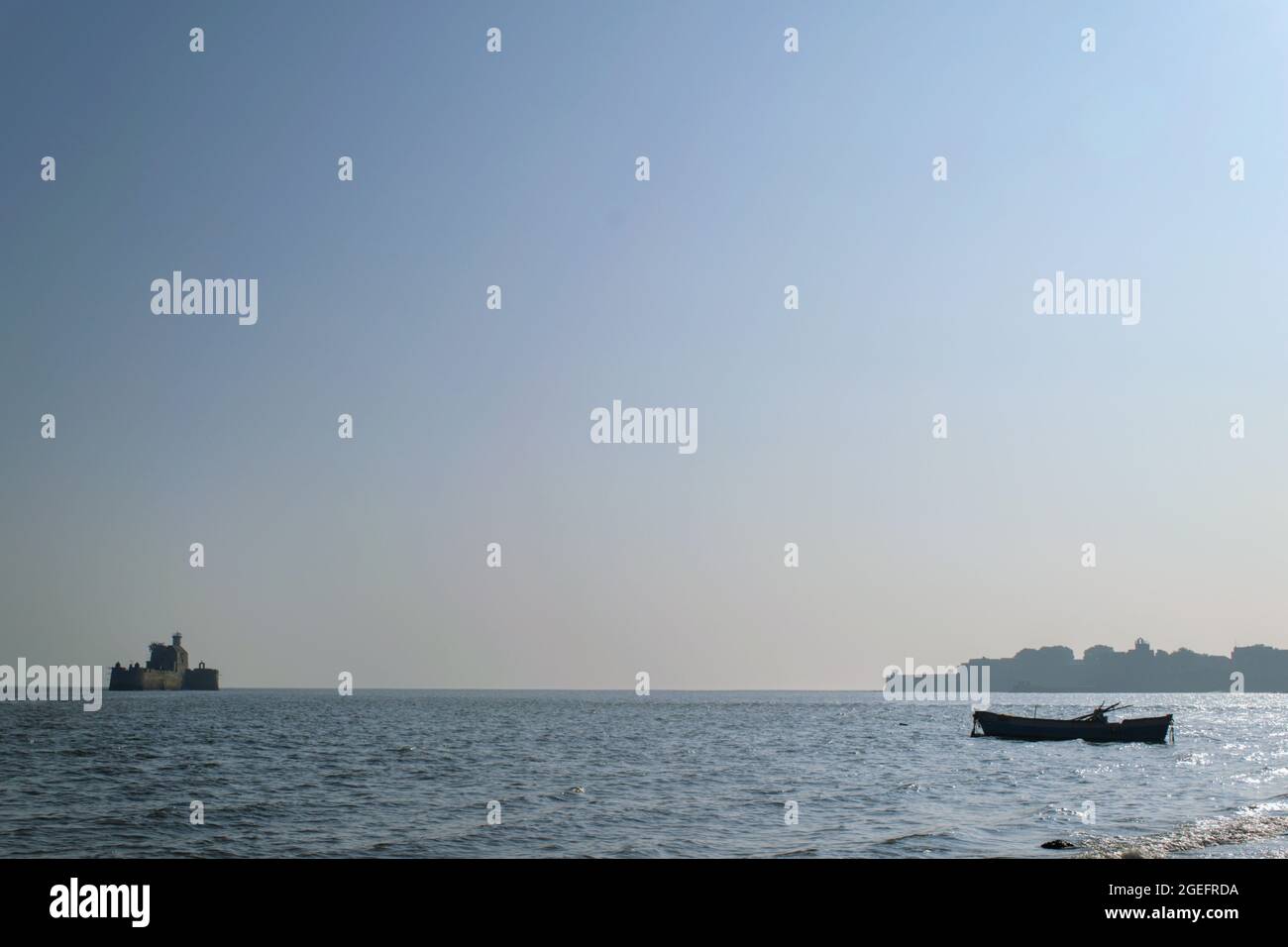 Silhouette of the boat, the Lighthouse and the City are visible on the bright sunny day, Diu, India. View of the Arabian sea on a bright summer day. Stock Photo