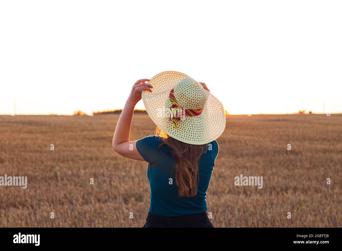 Adorable young girl in summer wheat field with straw hat in hands ...