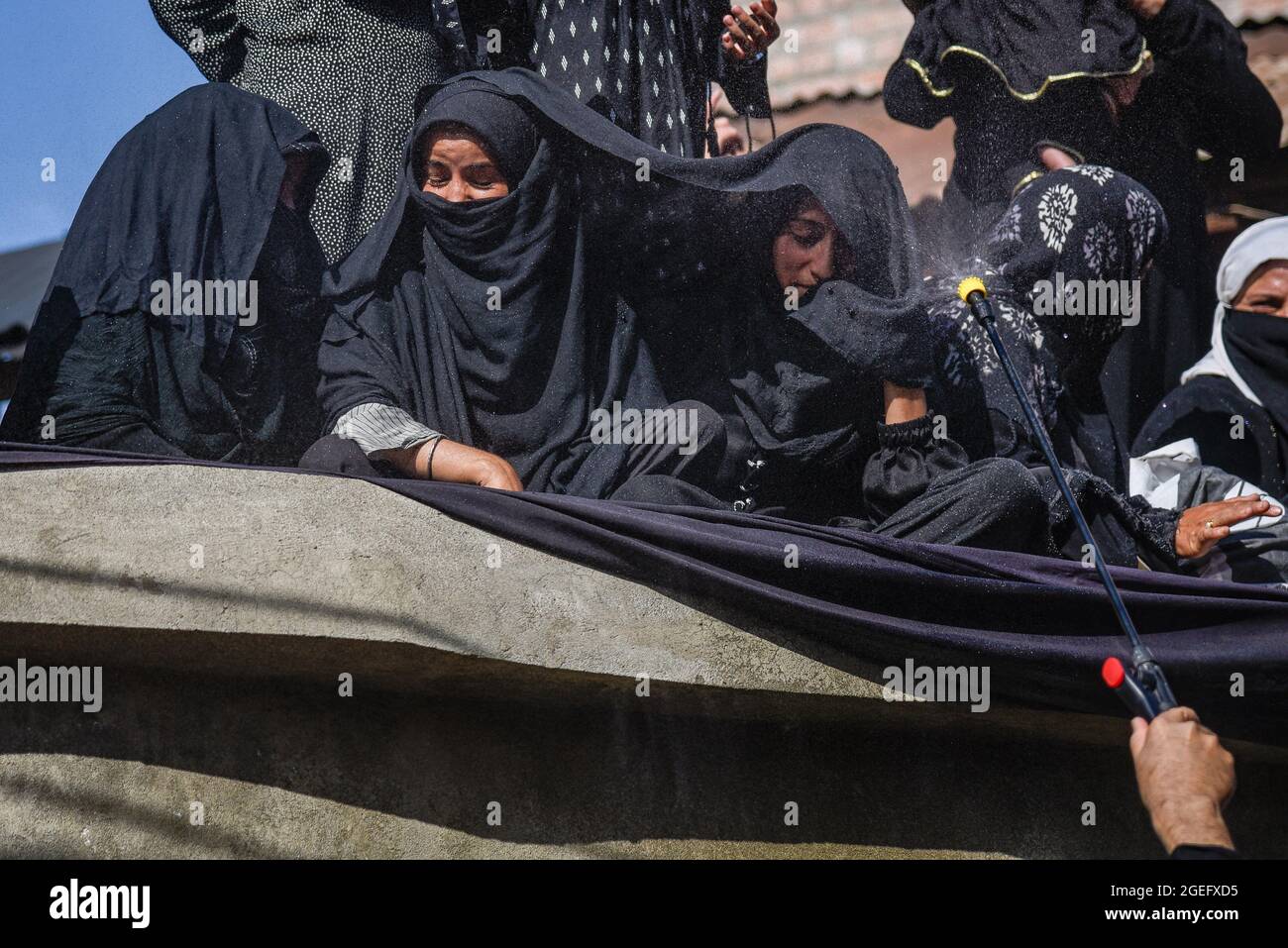 A Kashmiri Shia man (not framed) sprays rose water among the mourners ...