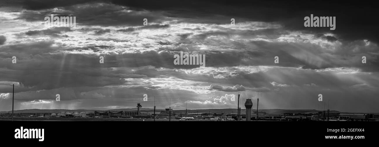 Panorama black and white image of frankfurt airport against impressive sky with wild cloud formations and sun rays Stock Photo