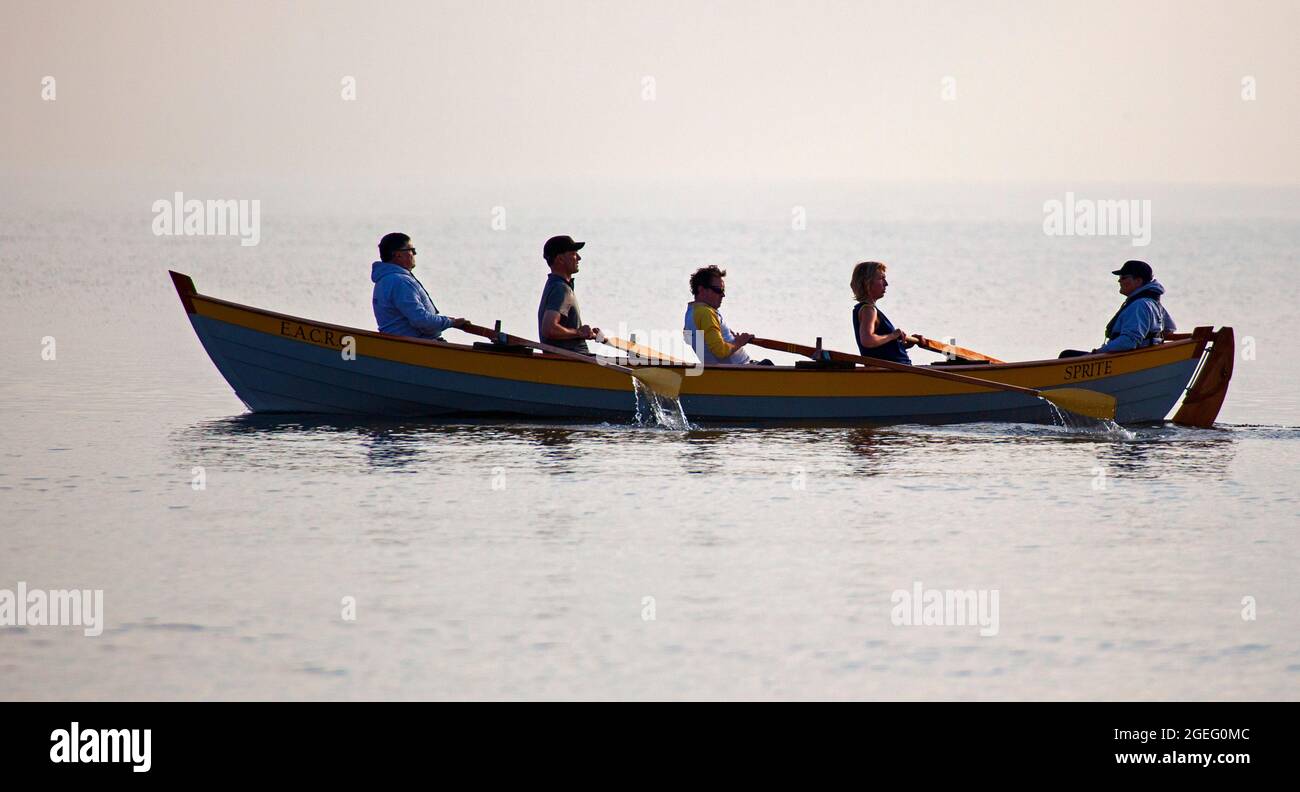 Portobello, Edinburgh, Scotland, UK weather. 20 August 2021 Hazy sunshine at  the seaside early morning before clearing up, temperature of 14 degrees for those out taking exercise.  Pictured: the mixed crew of Eastern Amateur Coastal Rowing Club out on the calm waters of the Firth of Forth with their boat Sprite. Credit: Scottishcreative/Alamy Live News. Stock Photo