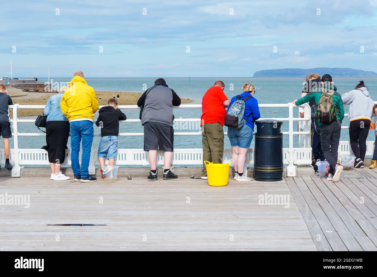 Tourists and visitors enjoying a summer afternoon fishing for crabs on Beaumaris Pier Anglesey North Wales Stock Photo