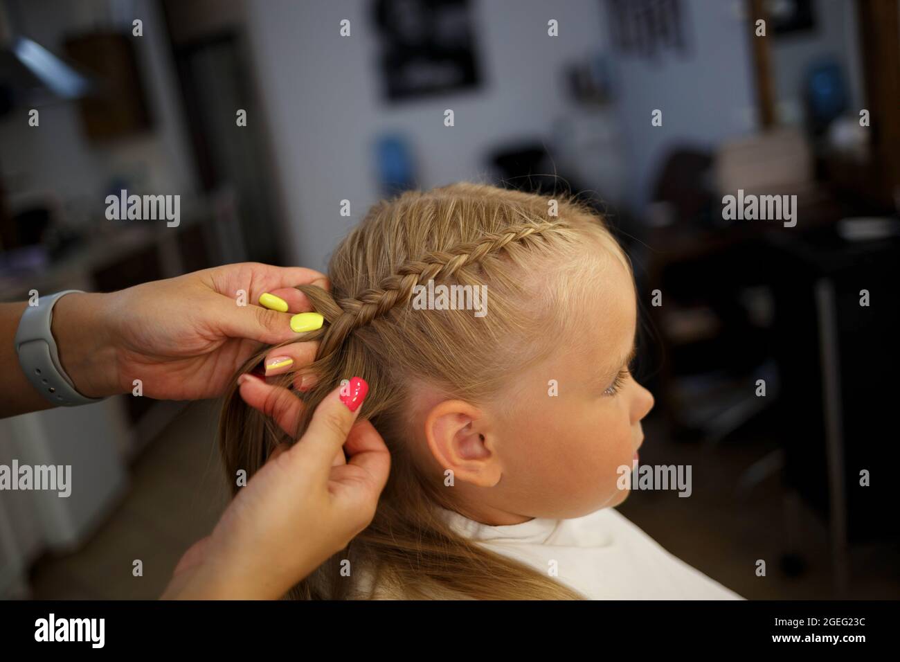 the little girl in the barber chair the hairdresser weaves a braid. Stock Photo