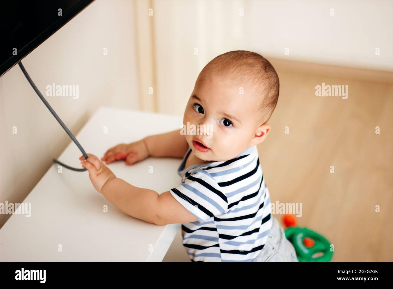 Sweet naughty baby boy pulls the electric cord from TV Stock Photo