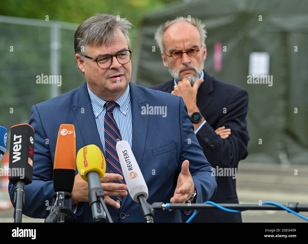 Doberlug Kirchhain, Germany. 20th Aug, 2021. Olaf Jansen, head of Brandenburg's Central Foreigners Authority, speaks at a press conference on the grounds of the DRK Refugee Aid in the initial reception facility. In the background is Markus Grünewald, State Secretary of the Brandenburg Ministry of the Interior. Early this morning, at around 4:30 a.m., two buses from the airport in Frankfurt am Main arrived here at the Central Foreigners Authority of Brandenburg with almost 59 local people from Afghanistan. Credit: Patrick Pleul/dpa-Zentralbild/dpa/Alamy Live News Stock Photo
