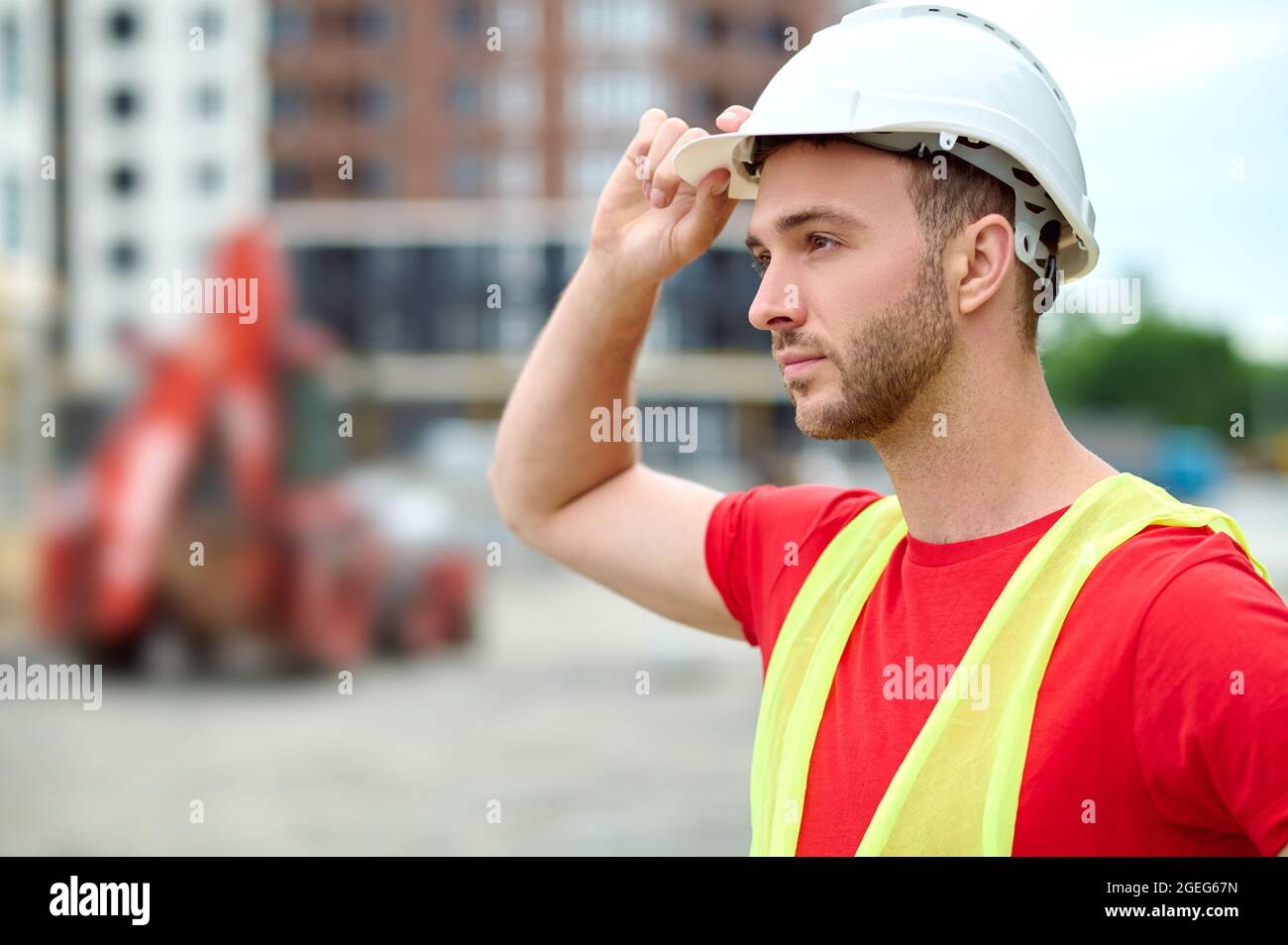 Serene bearded construction worker touching his protective helmet Stock Photo