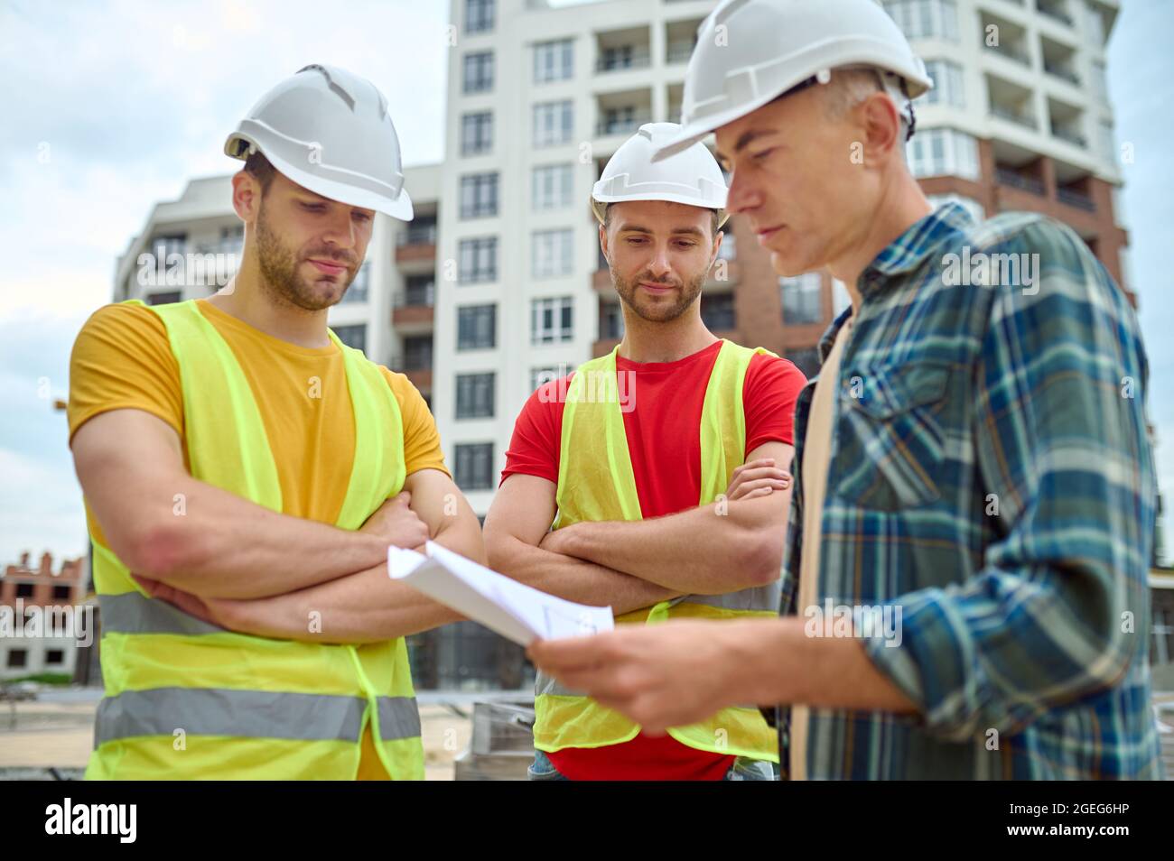 Three Caucasian workers in headwear analyzing technical drawings Stock Photo