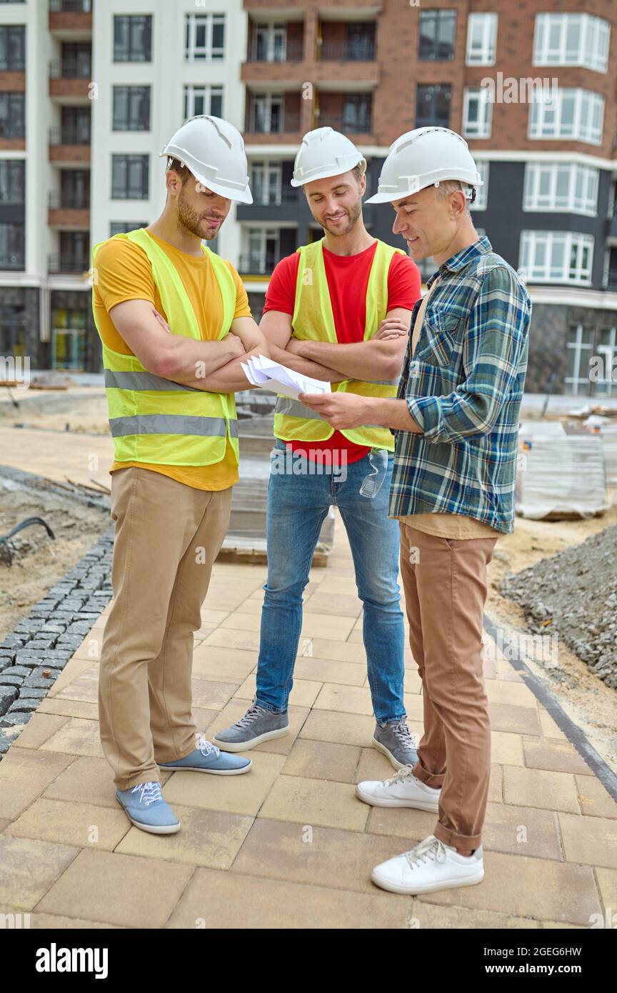 Three men in protective helmets analyzing technical drawings Stock Photo