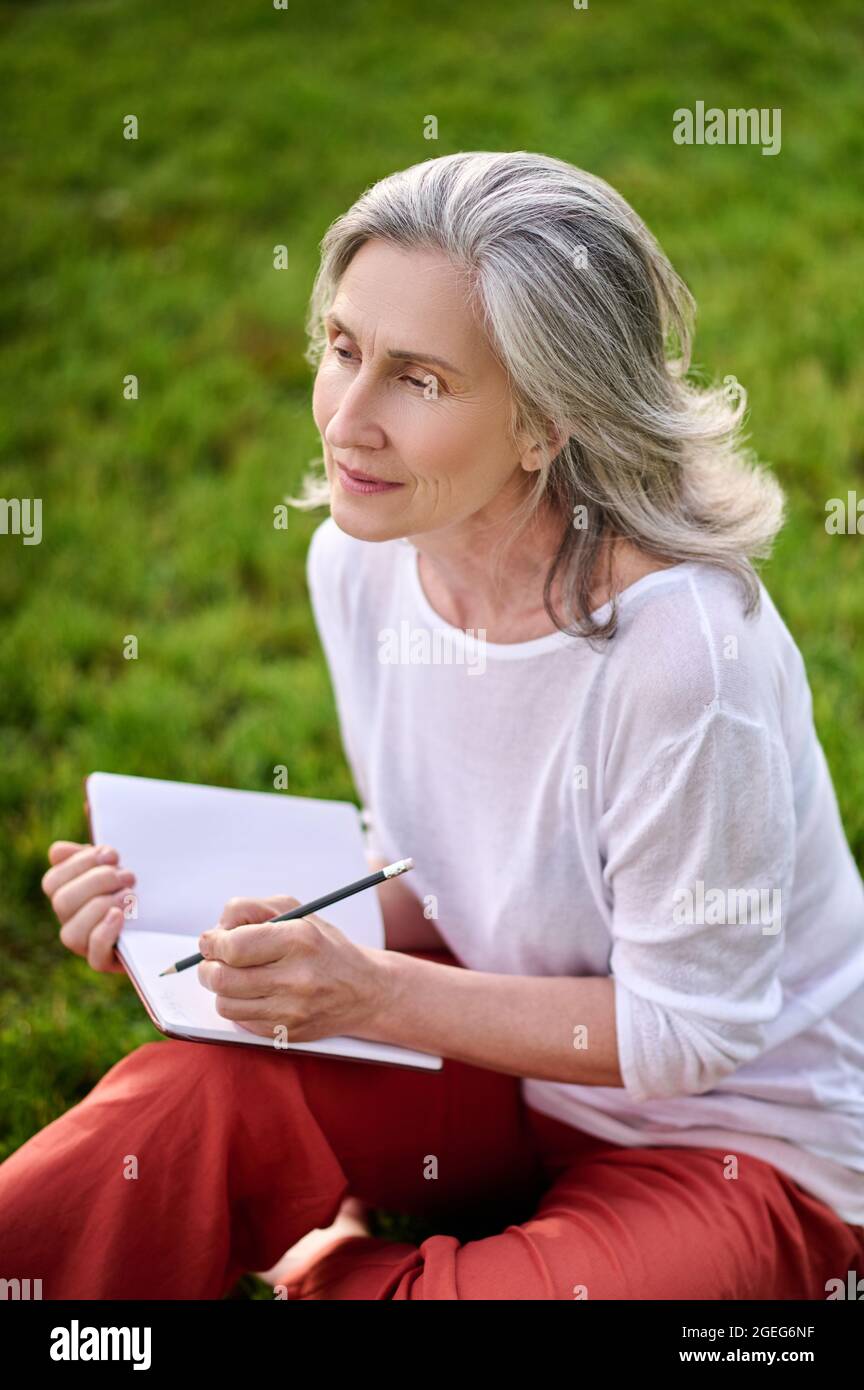 Gray-haired woman with notepad with pensive look Stock Photo