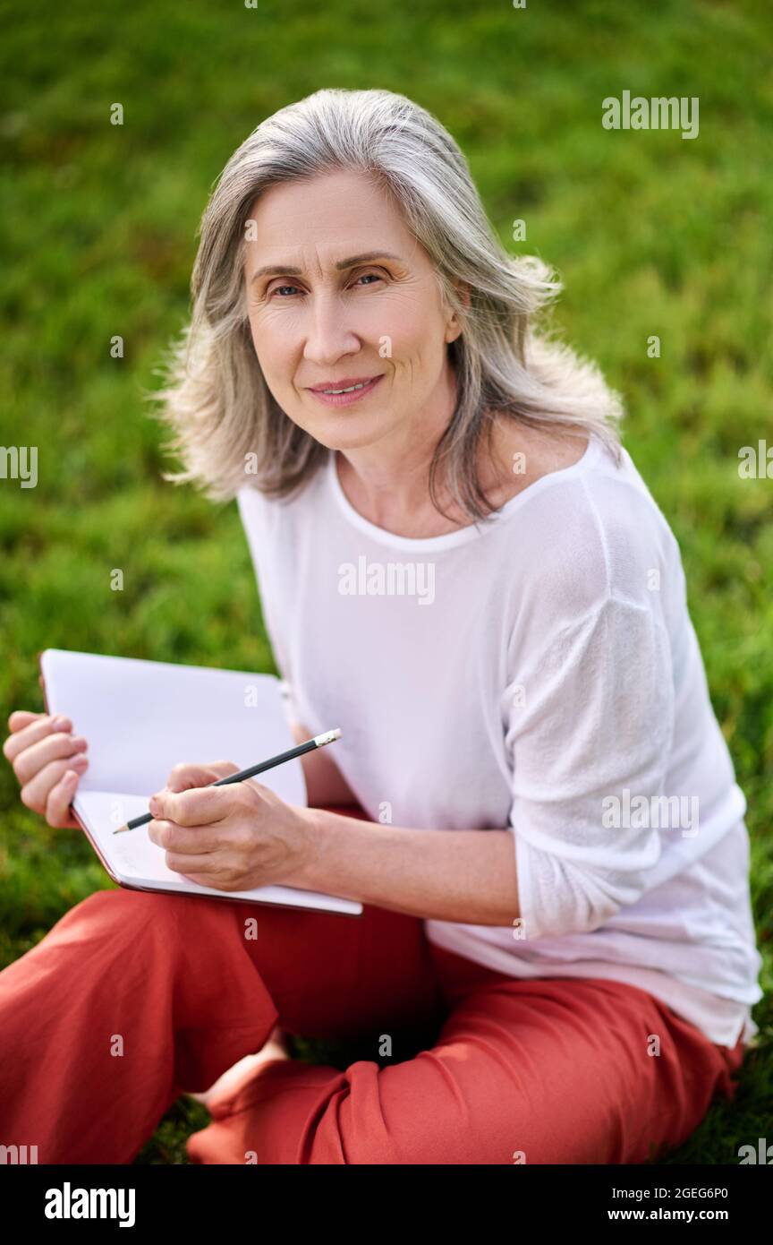Woman with notebook and pencil sitting on grass Stock Photo