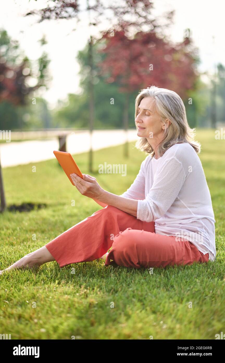 Woman looking attentively at tablet sitting on lawn Stock Photo
