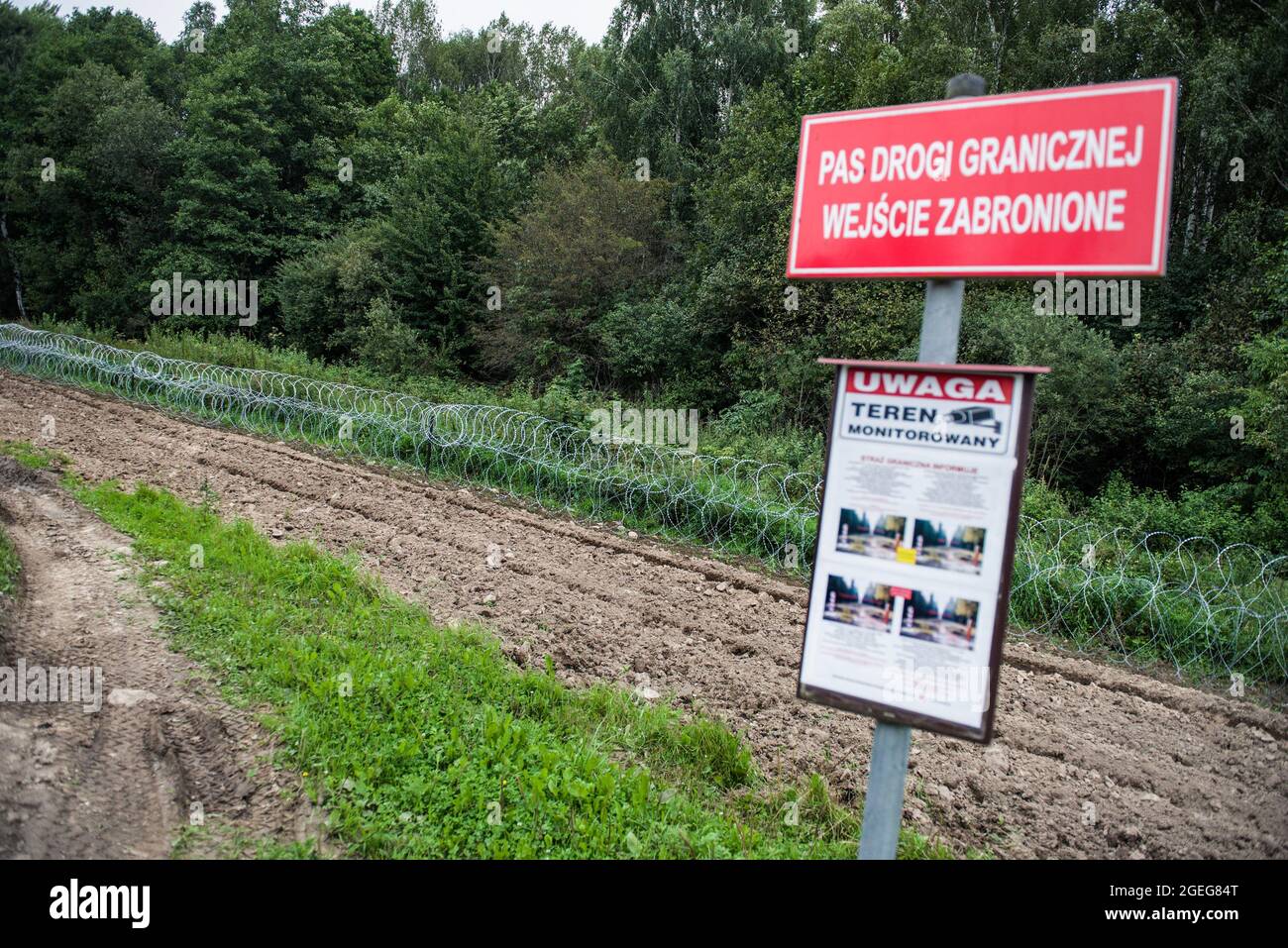 Newly build barbed wired fence in the fields is seen at the Polish-Belarusian border and a sign that reads 'border strip, entry is forbidden'. The growing number of people trying to cross into Poland is turning migration into a domestic political issue in Poland. In a border village Usnarz Gorny there is a stand-off between Belarusian and Polish border guards with more than 30 Afghan refugees stuck in the middle. The refugees stuck there since almost two weeks as they are not allowed to enter Poland or return to Belarus. Poland has deployed hundreds of troops along its border with Belarus to s Stock Photo