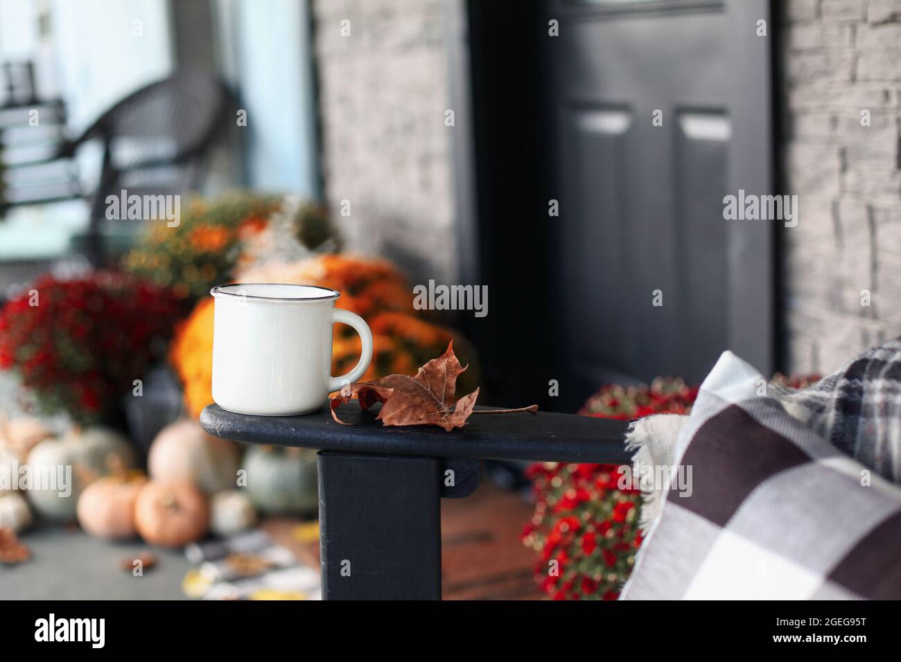 Steaming coffee cup sitting on arm of rocking chair on a front porch that has been decorated for autumn with heirloom white, orange and grey pumpkins Stock Photo