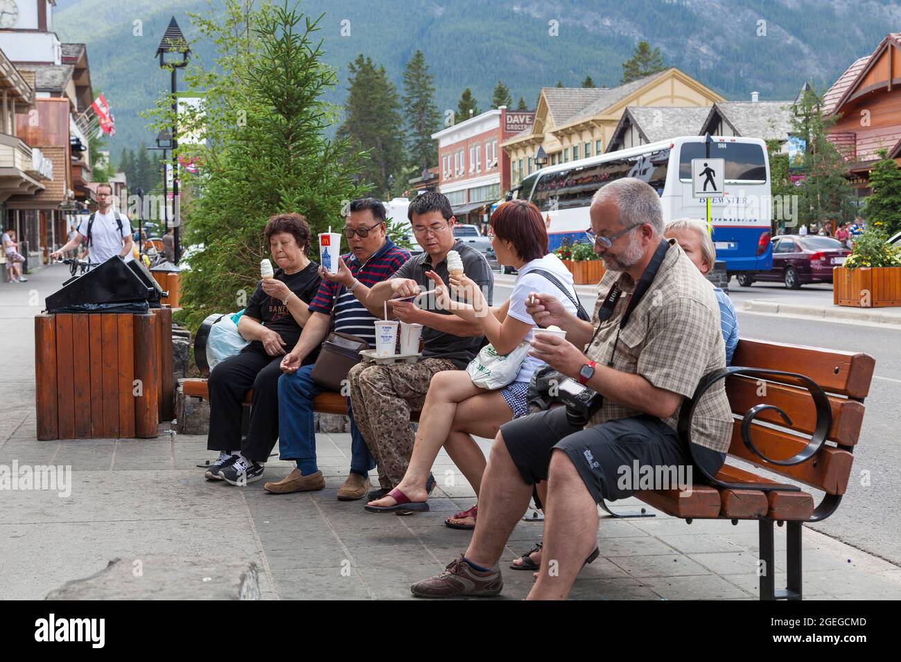 Tourists sitting on a bench on the Banff avenue and eating ice cream ...