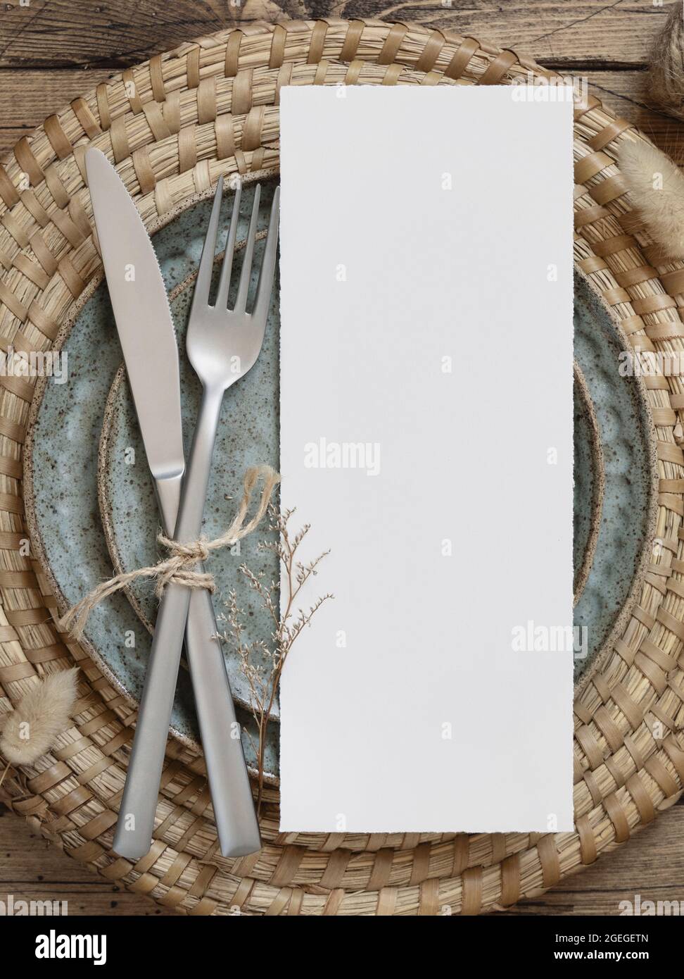 Blank menu card on plate with fork and knife on wooden table with bohemian decorations and dried plants, top view. Boho wedding card mockup Stock Photo