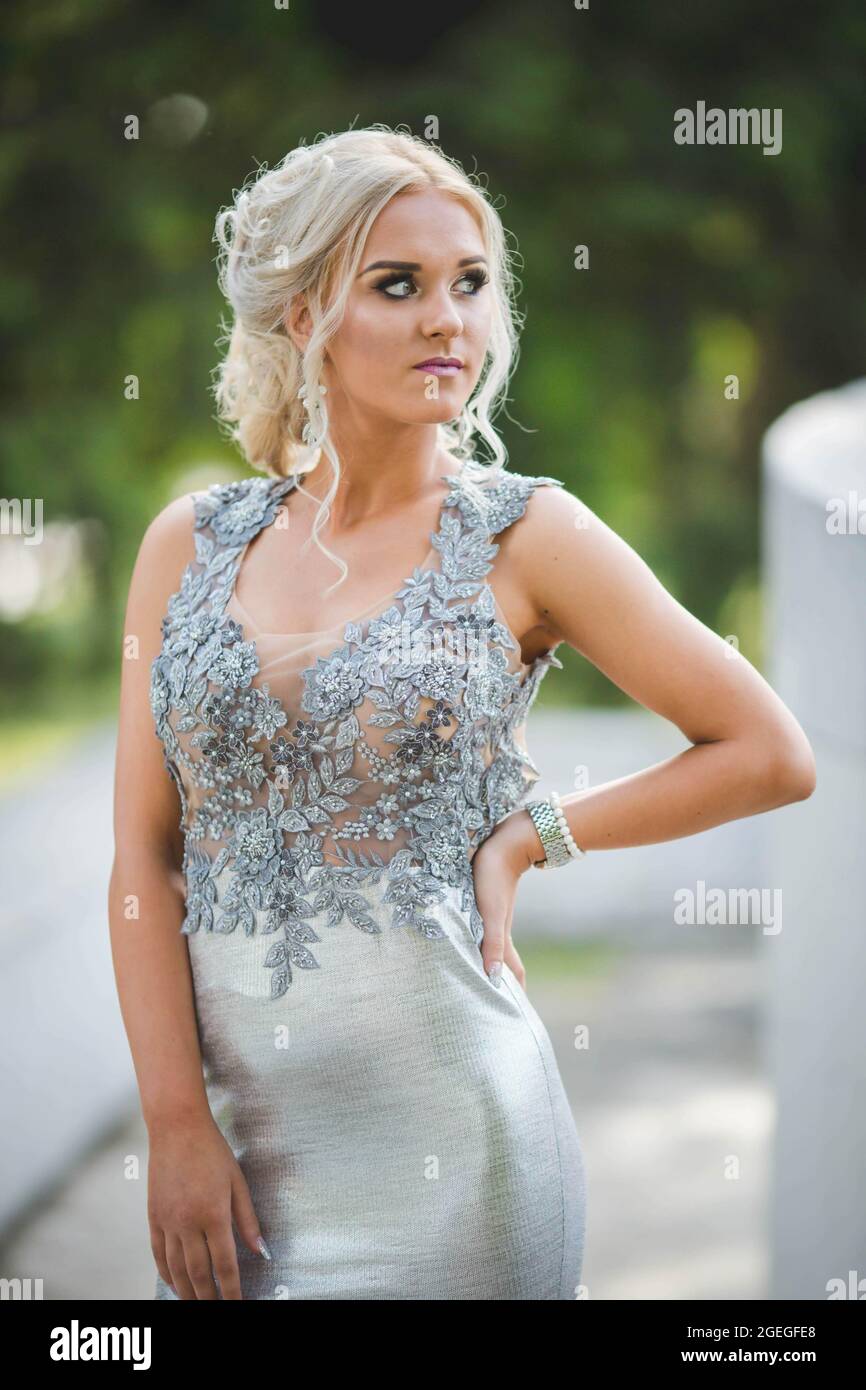 Young blonde lady wearing a long silver dress with lace is posing outdoors  Stock Photo - Alamy