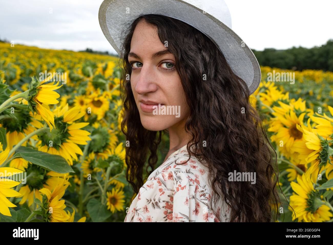 Smiling young woman standing in the middle of a field of sunflowers ...