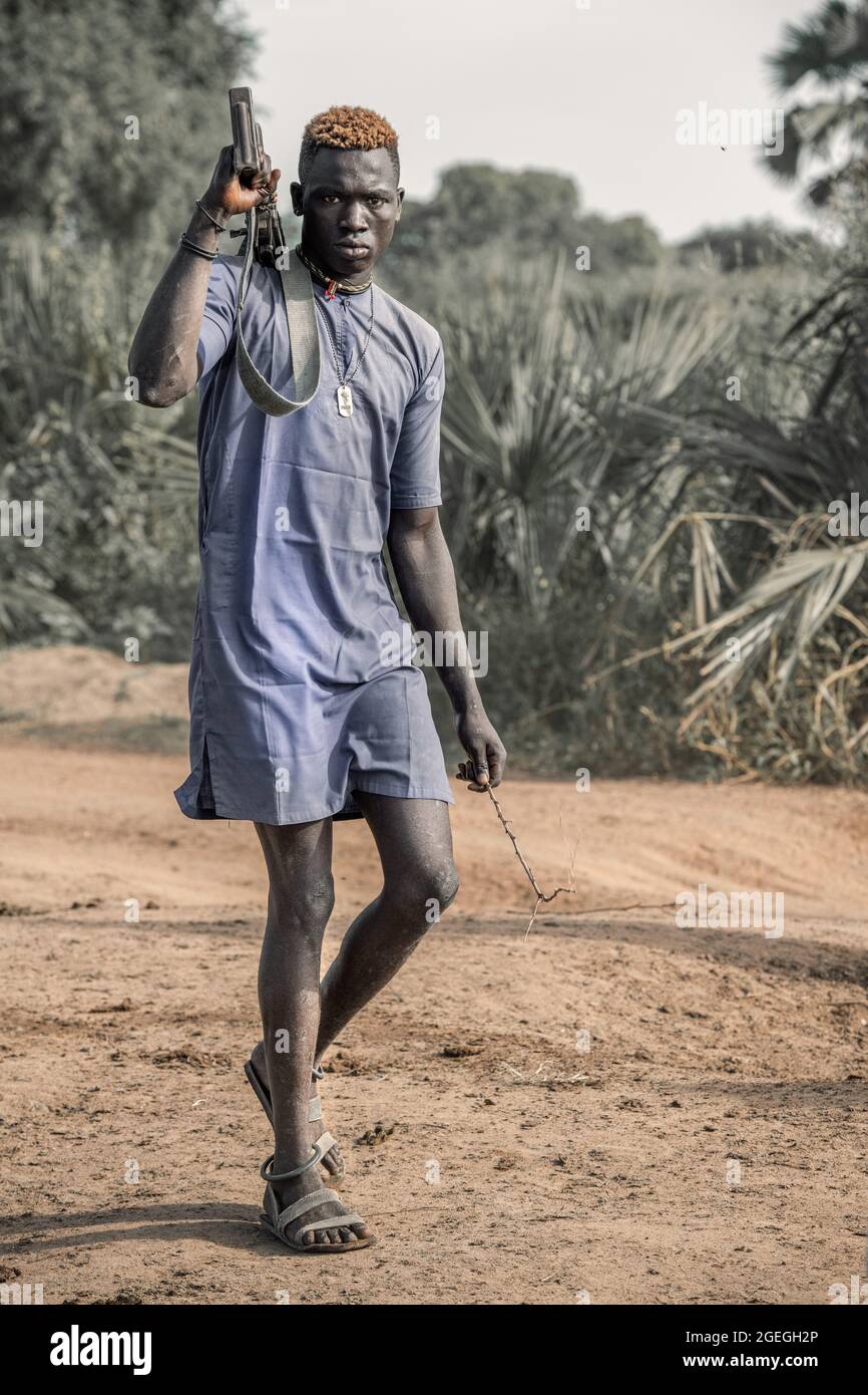 A man looked straight into the camera as he walked past, holding his gun casually behind his back. TEREKEKA, SOUTH SUDAN: In one image, a man stared i Stock Photo