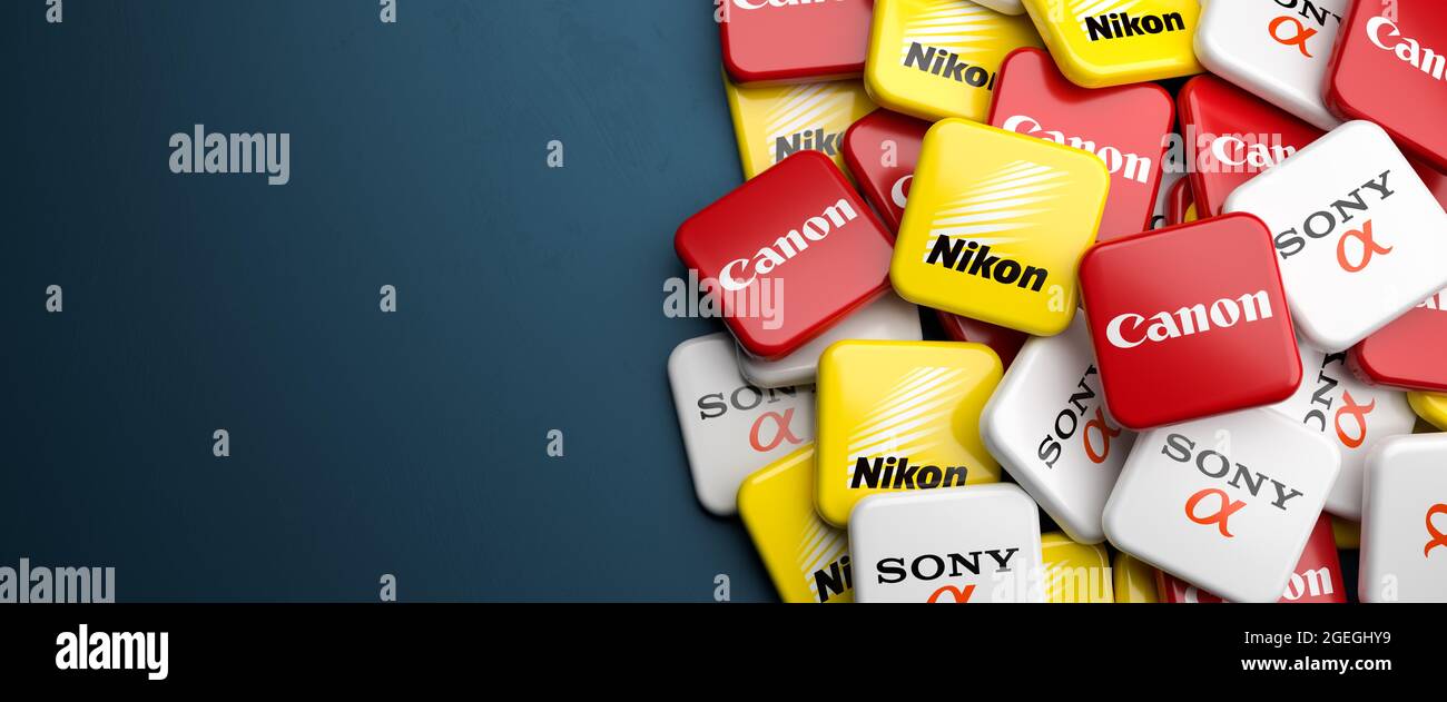 Logos of the competing Japanese optics and camera companies Sony (Alpha), Nikon and Canon on a heap on a table. Copy space. Web banner format. Stock Photo