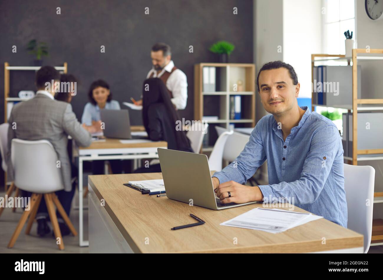 Young smiling office worker is typing on a laptop, working on a project Stock Photo