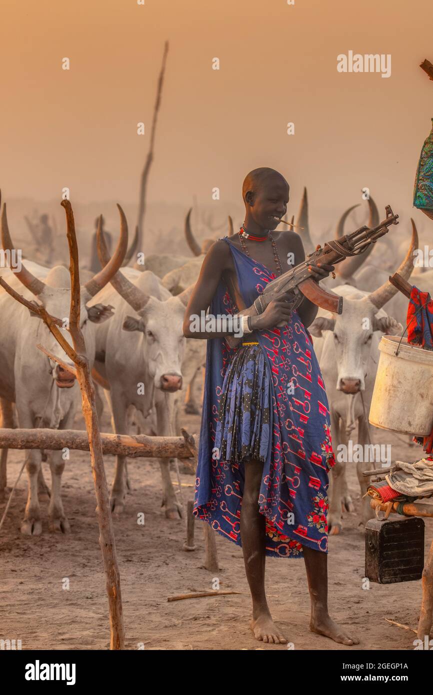 A woman held an AK47 casually out in front of her. TEREKEKA, SOUTH SUDAN: In one image, a man stared into the camera surrounded by cows while brandish Stock Photo
