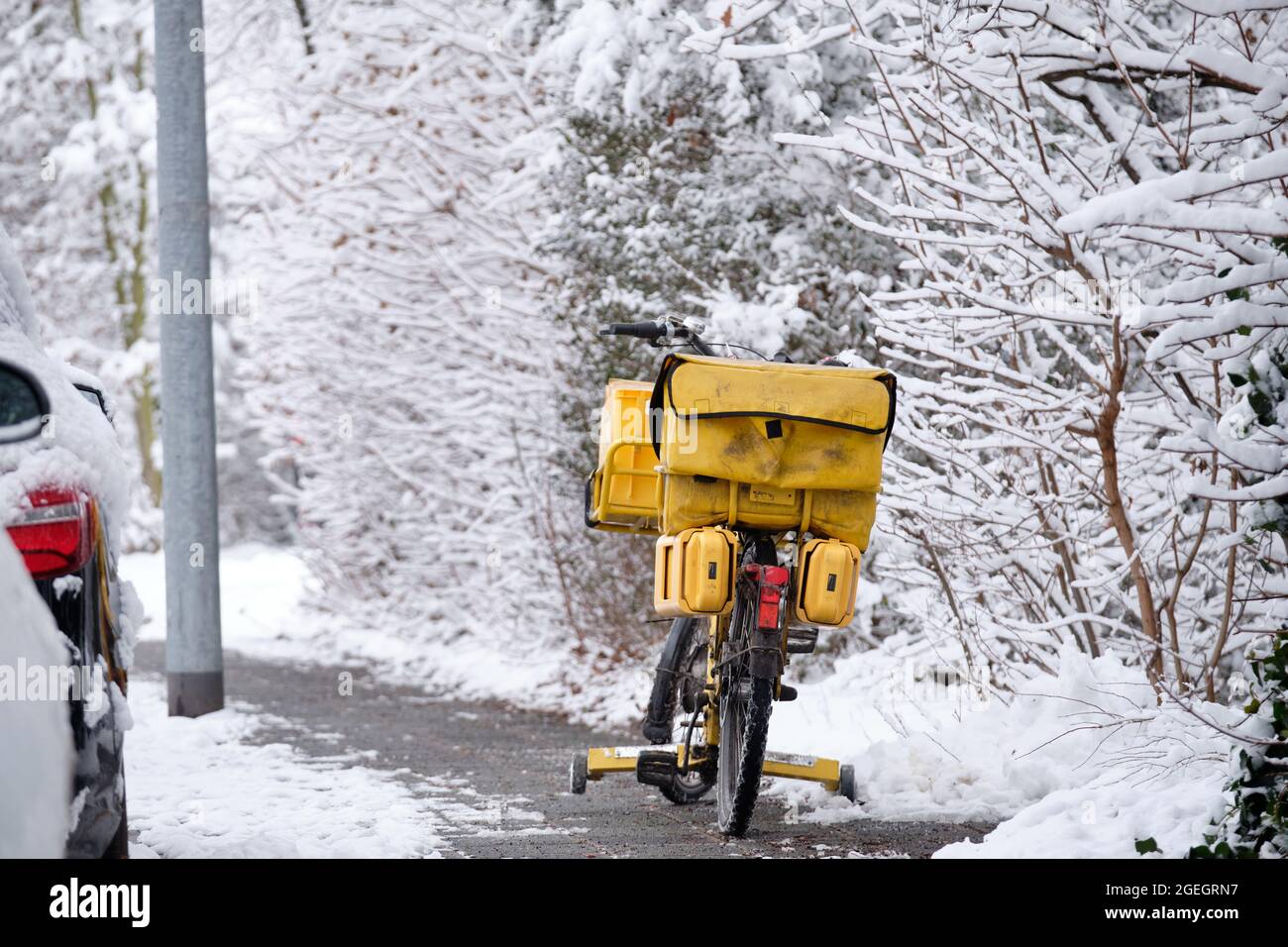 Nuremberg, Germany - February 08, 2021: A postman's yellow bicycle with panniers for the post is standing on a snow covered winter pavement while the Stock Photo