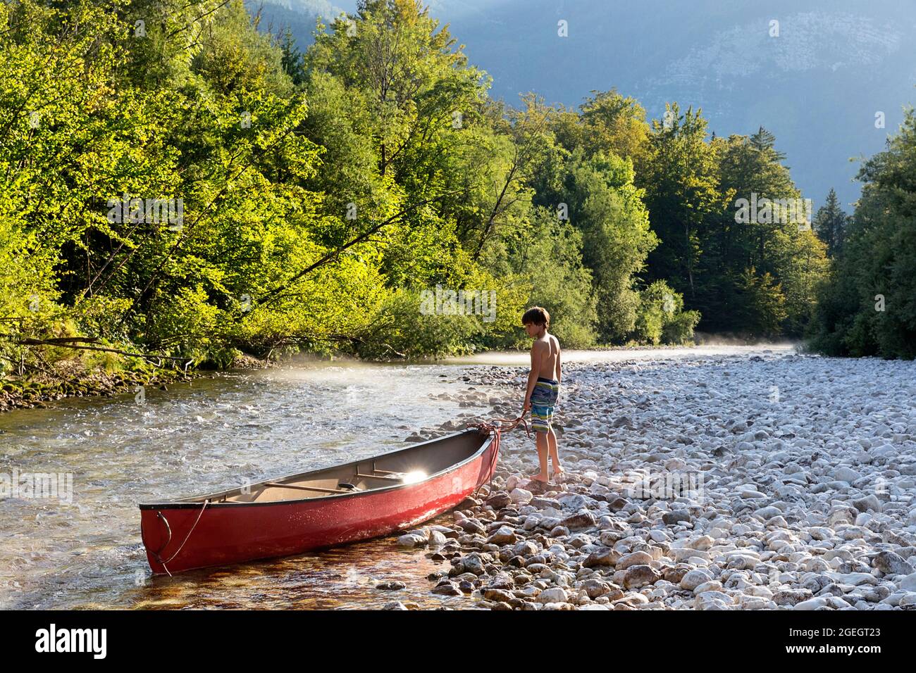Boy looking after beautiful red canoe on Sava Bohinjka river just before lake Bohinj, Slovenia Stock Photo