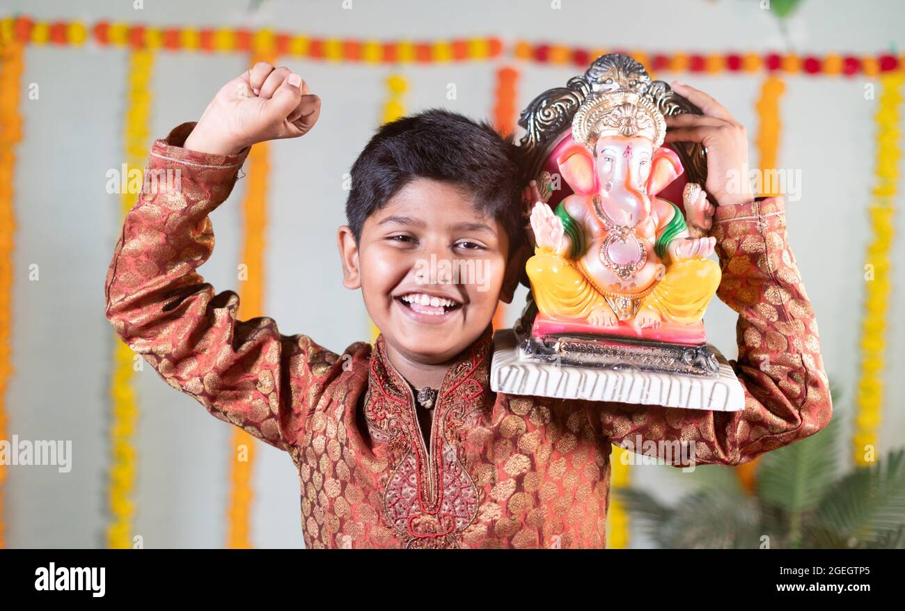 Happy smiling kid with ganesha idol on shoulder saying or chanting ganapati bappa morya during festival celebrations Stock Photo