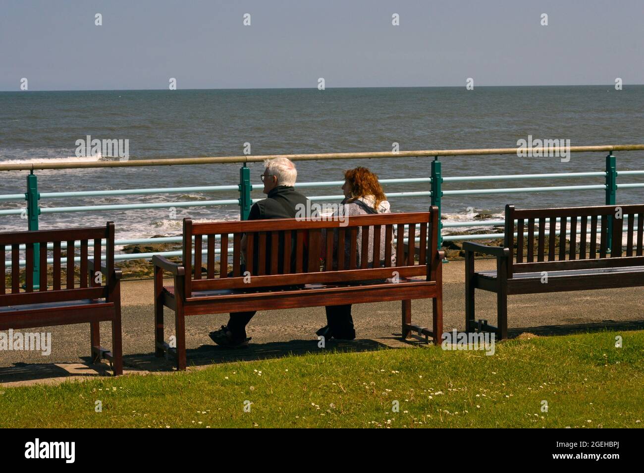 WHITLEY BAY. TYNE and WEAR. ENGLAND. 05-27-21. A man and woman seated on a bench on the promenade, overlooking the beach and North Sea. Stock Photo