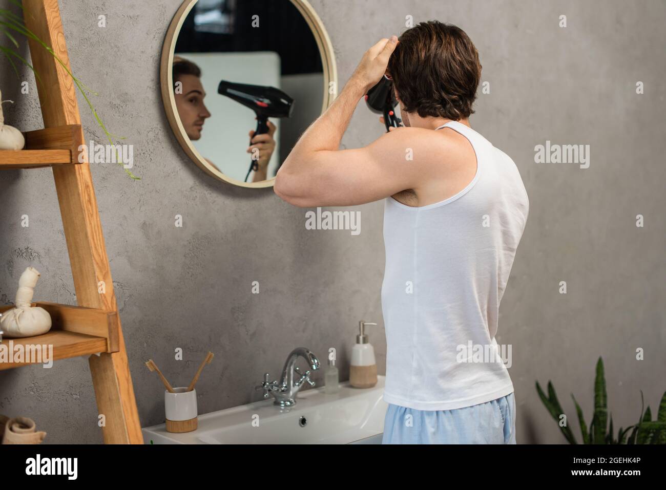 man in white tank top drying hair near mirror in bathroom Stock Photo -  Alamy