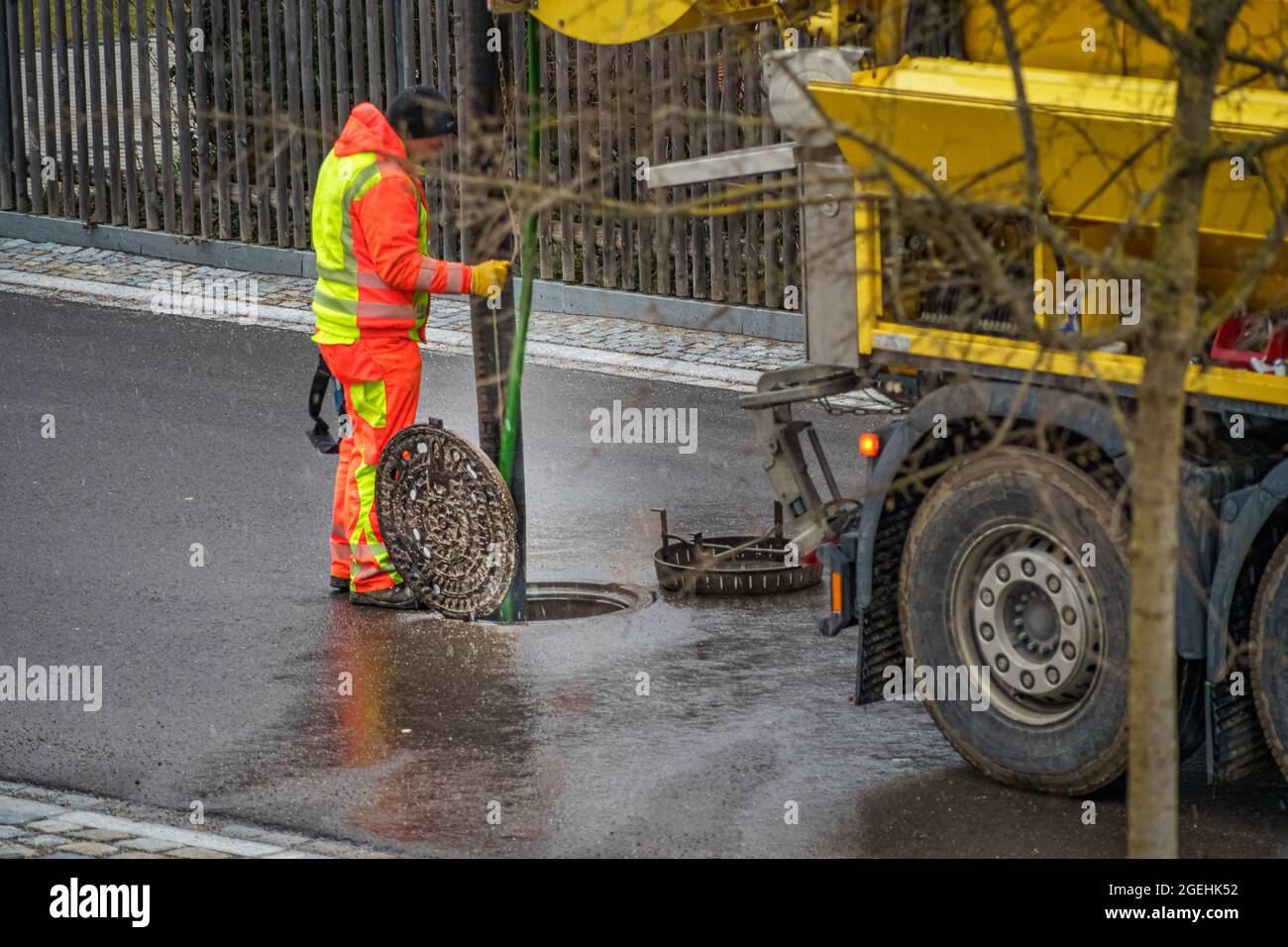 Maintenance at a manhole with a unrecognizable man, working behind the sewer cleaning vehicle on the open street. Stock Photo